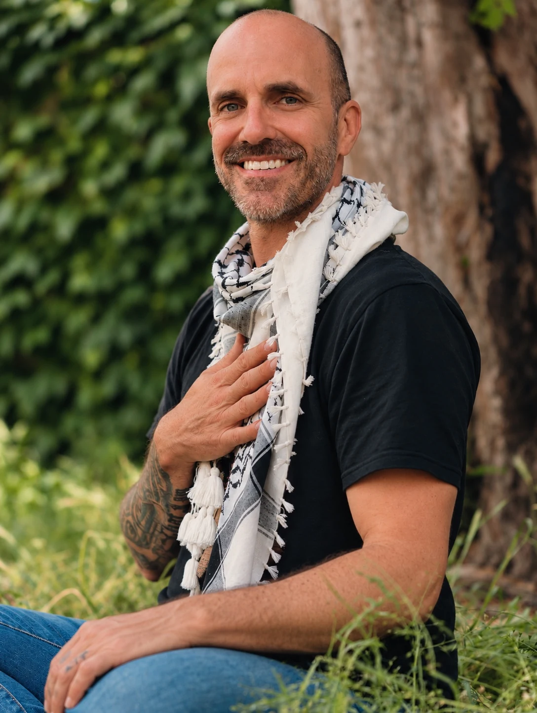 Will smiling outdoors beside a tree, with one hand resting on his chest
